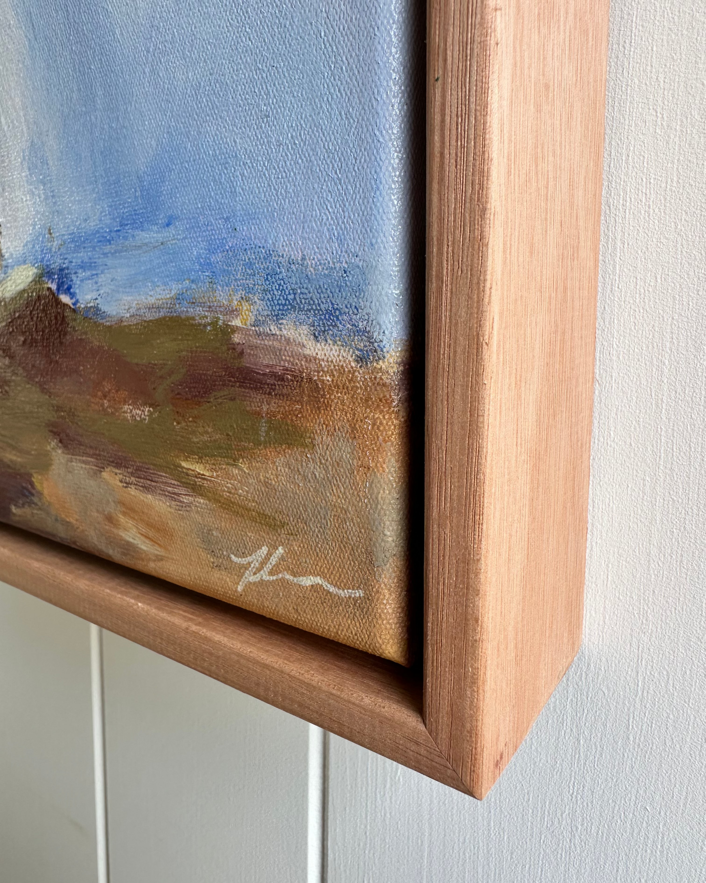 Close-up of a painting with a wooden frame on a white wall.
