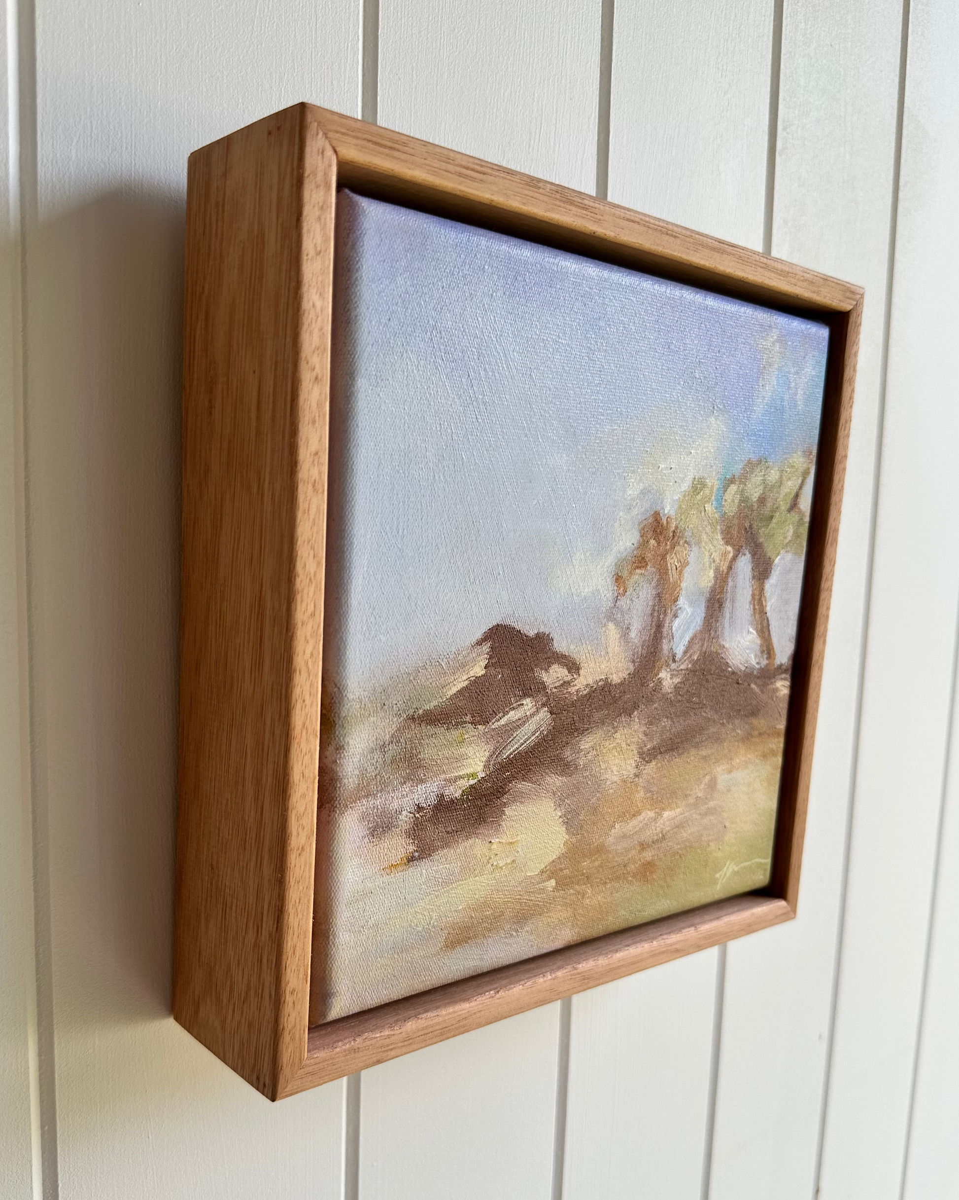 Framed painting of a landscape with trees on a wall.