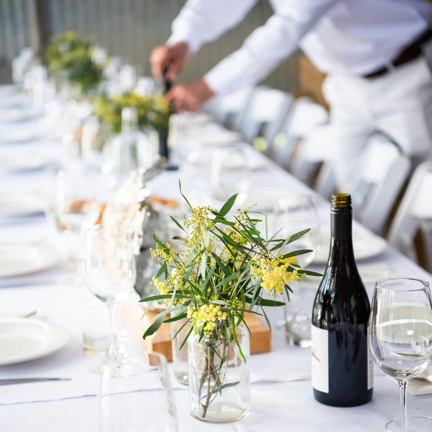 Long table set for a meal with white tablecloth, plates, glasses, and centerpieces.