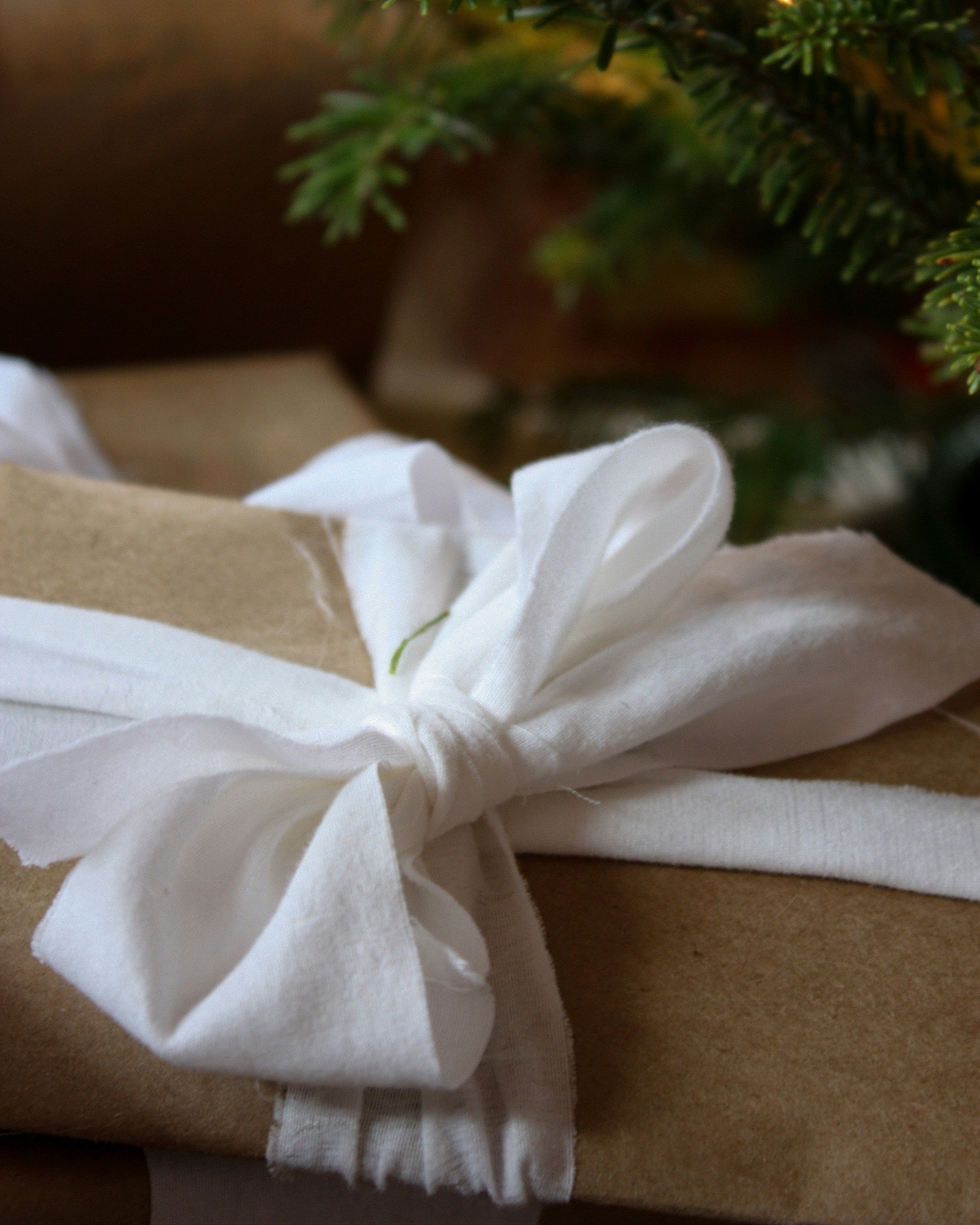 Gift wrapped in brown paper with a white bow, Christmas tree in the background