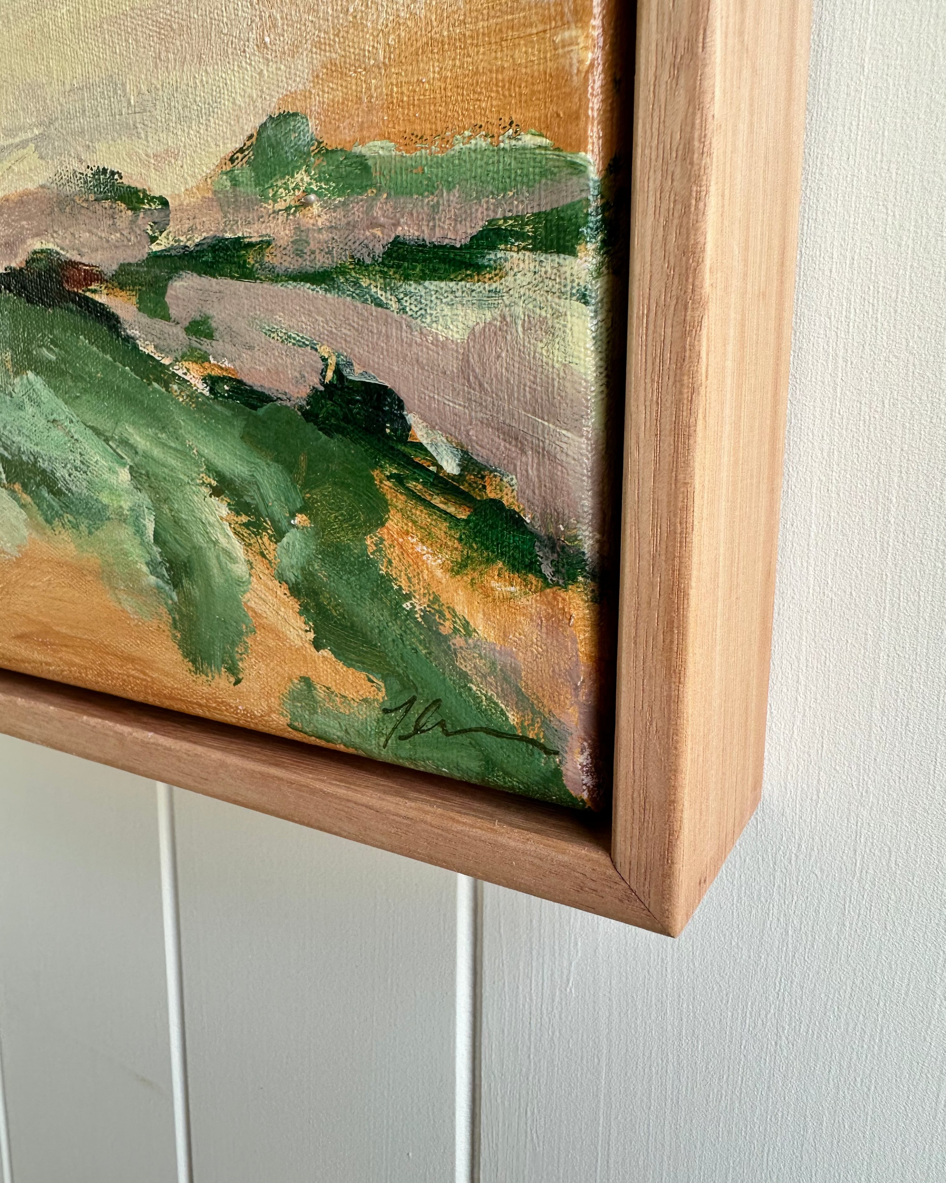 Close-up of a landscape painting with a wooden frame on a white wall.